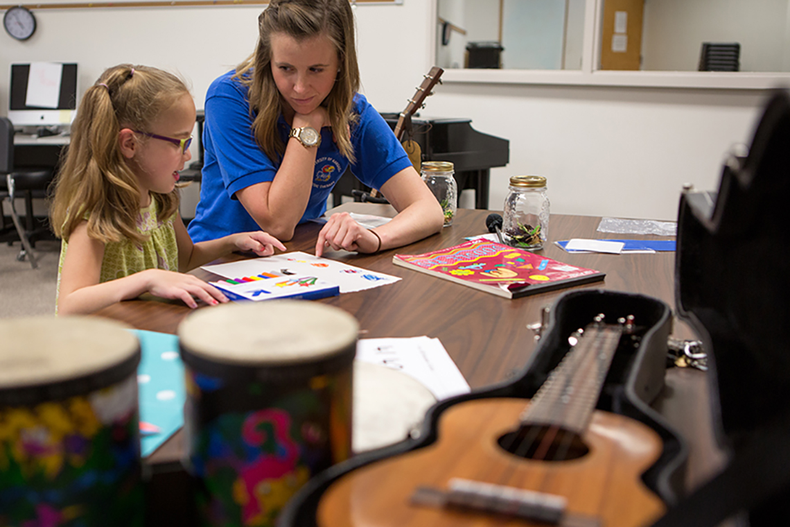 A teacher works with a young student and points at a piece of paper while in a room with instruments