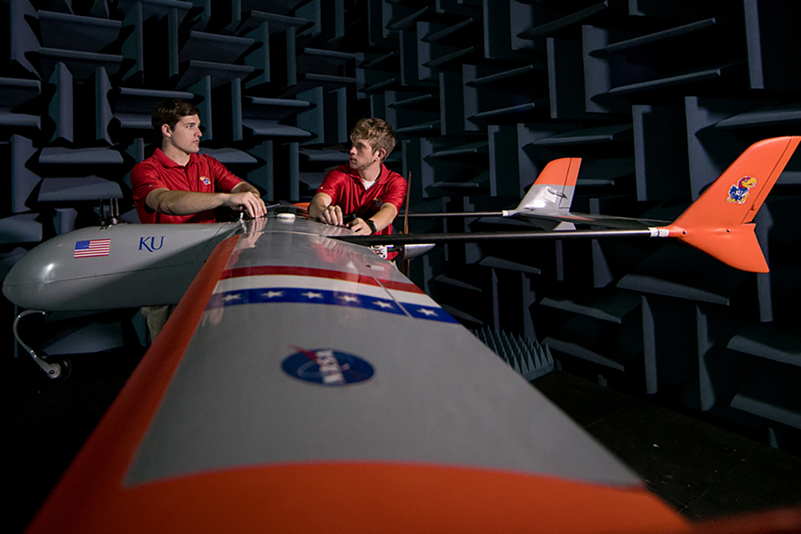 Two researchers discuss while standing next to a KU-designed small airplane