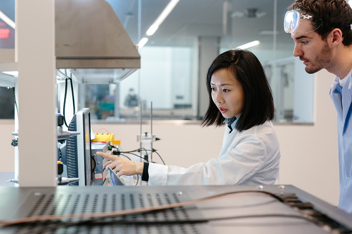 A professor helps a student researcher in a lab, pointing to a computer screen