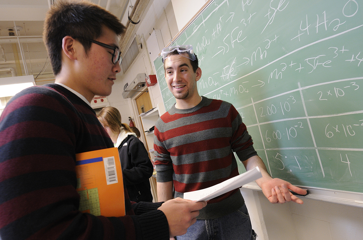 A graduate teaching assistant helps a student next to a chalkboard full of equations