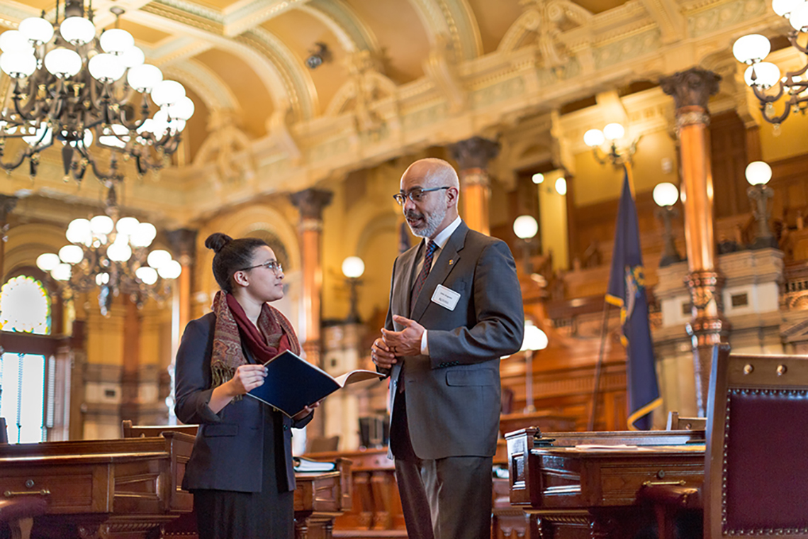 Two people speak in the Kansas State Capitol. One holds a folder