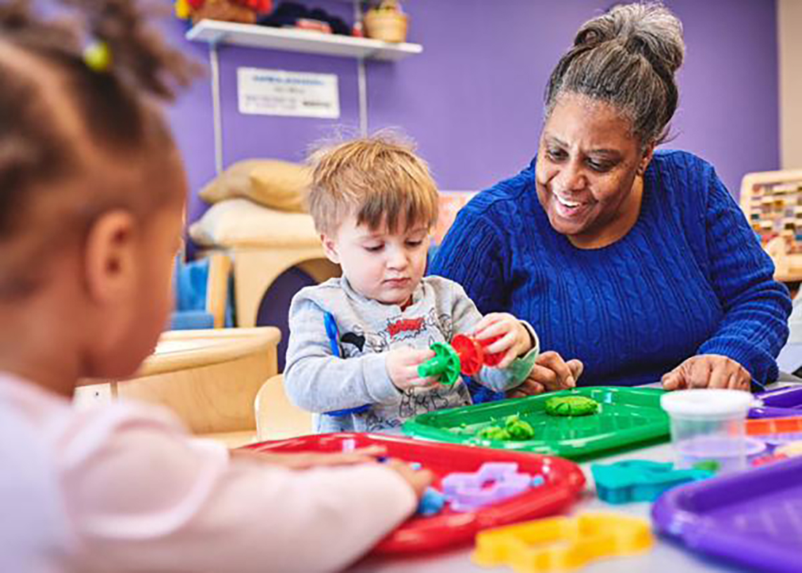 A teacher works with students who play with play-doh 