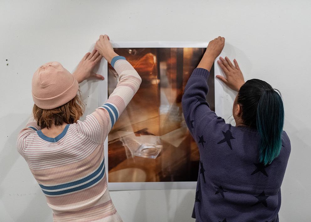 Two students hang a large piece of artwork on the wall